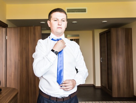 Portrait of  handsome businessman in suit putting on necktie indoors.の写真素材