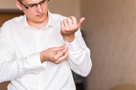 Business man fastening buttons on shirt sleeve at home.