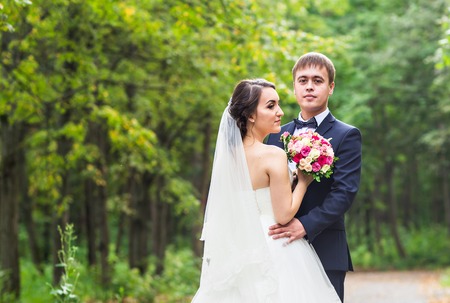 Bride and groom at wedding Day walking Outdoors on spring nature. Bridal couple, Happy Newlywed woman and man embracing in green park. Loving wedding couple outdoor. Bride and groomの写真素材