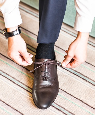 A young man tying elegant shoes indoors.の写真素材