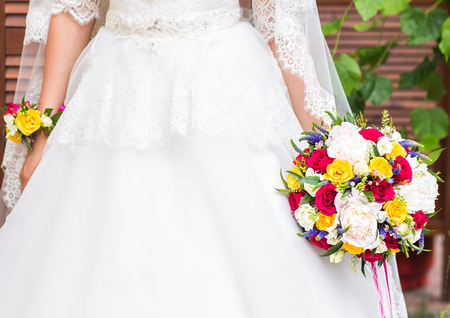 beautiful bouquet of different colors in the hands of the bride in a white dressの写真素材