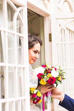 beautiful bouquet of different colors in the hands of the bride in a white dressの写真素材