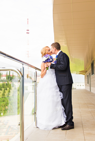 Handsome brunette groom kissing beautiful bride in wedding dress with bouquet bridesmaids in backgroundの写真素材