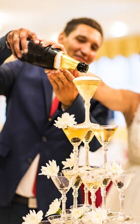 Bride and groom pouring champagne into the glass. Pyramid of champagne.の写真素材