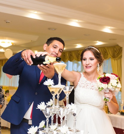 Bride and groom pouring champagne into the glass. Pyramid of champagne.の写真素材