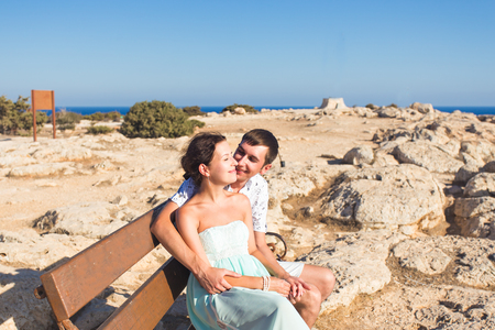 love couple sitting outdoors on a bench looking the sea and sky in background.の写真素材