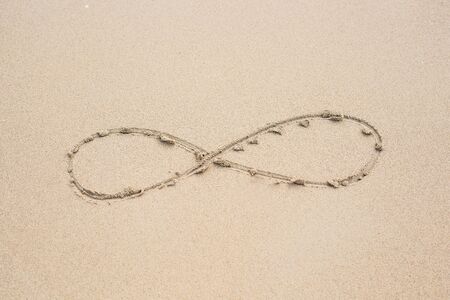 infinity symbol written on sand. Summer beach background.の写真素材