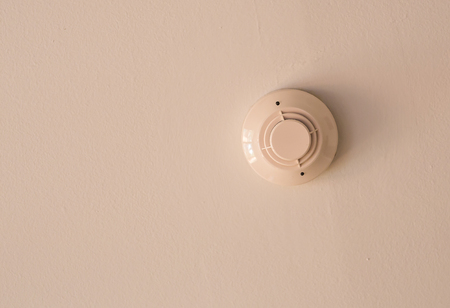 White smoke detector on a white ceiling.