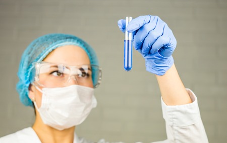 Close-up of glass tube with blue fluid in nurse hand during medical test.の写真素材
