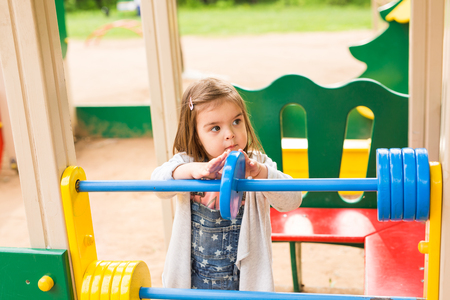 Little girl on a playground. Child playing outdoors in summer. Kids play on school yard. Happy kid in kindergarten or preschool. Children having fun at daycare play ground. Toddler on a swing.の写真素材