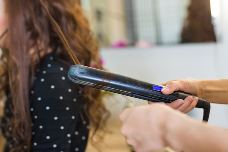 Close up of stylist's hand using curling iron for hair curlsの写真素材
