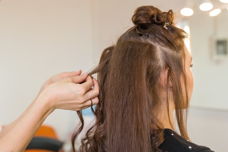 Closeup hairdresser coiffeur makes hairstyle for young womanの写真素材