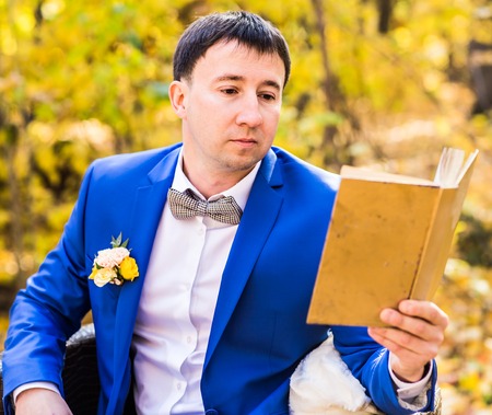 Young man reading a book in the autumn park