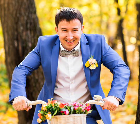 Handsome groom and Vintage Bicycle with flowers on autumn landscape background.の写真素材