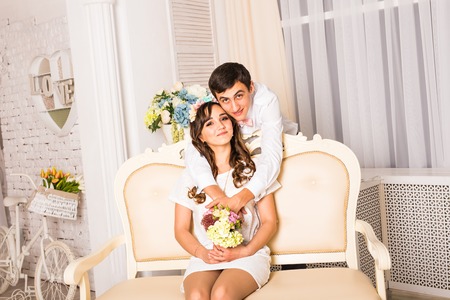 happy stylish couple hugging and sitting on background of luxury interior in studioの写真素材