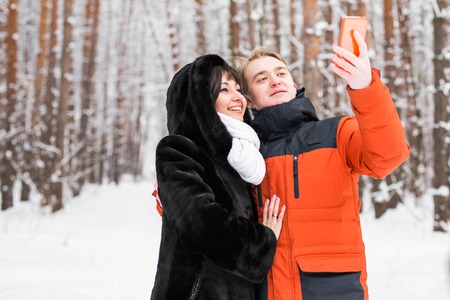 people, season, love, technology and leisure concept - happy couple taking picture with smartphone...