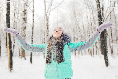 Girl playing with snow in park. Happy young woman having fun in the snowの写真素材