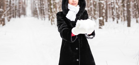 Young woman in the snow mountains landscape on holiday holding natural soft white snow in her hands to make a snowball, smiling during a cold winter day in the forest, outdoors.の写真素材
