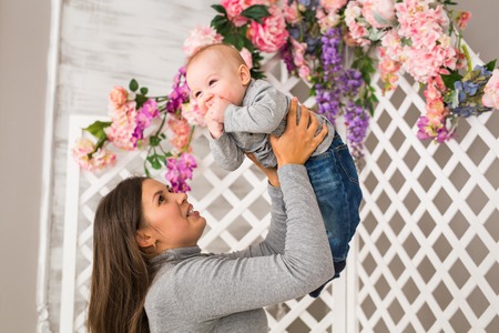 Young mother holding her newborn child. Mom nursing baby. Woman and new born boy in white bedroom with rocking chair and blue crib. Nursery interior. Mother playing with laughing kid. Family at homeの写真素材