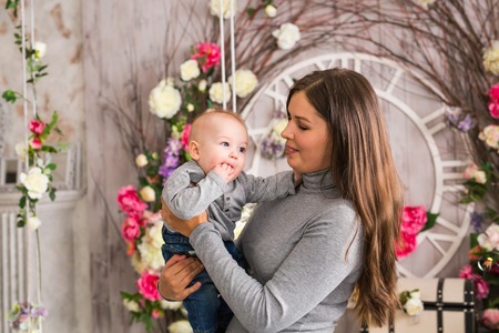 Young mother holding her newborn child. Mom nursing baby. Woman and new born boy in white bedroom with rocking chair and blue crib. Nursery interior. Mother playing with laughing kid. Family at homeの写真素材