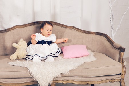 happy little baby girl sitting on the couch with teddy bear toy.