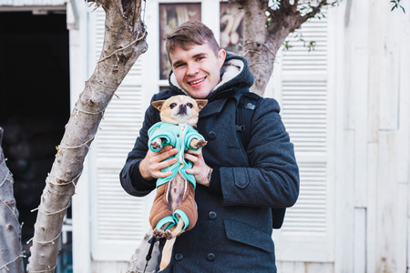 Portrait of handsome young man holding a cute chihuahua dog outdoorの写真素材