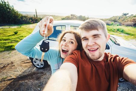 Young funny couple with keys to new car outdoorの写真素材