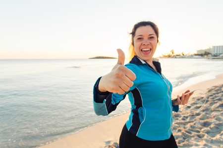 Concept of sport, fitness, healthy lifestyle and running - Motivated sporty woman doing thumbs up success gesture after outdoors workout at the beachの写真素材