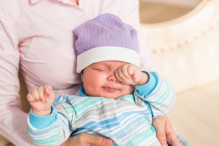 Portrait of newborn tired baby boy rubbing eyesの写真素材