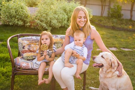 Mother and her children Relaxing In Garden With Pet Dog. Happy family playing with their labrador retriever dog on a sunny dayの写真素材