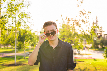 Fashion, people and lifestyle concept - Close-up portrait of happy cheerful confident handsome man in sunglasses in parkの写真素材