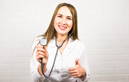 Happy female doctor using stethoscope and gesture thumbs upの写真素材