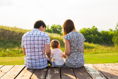weekend, children and parenthood concept - Family sitting on the wooden surface and looking at the beautiful summer viewの写真素材