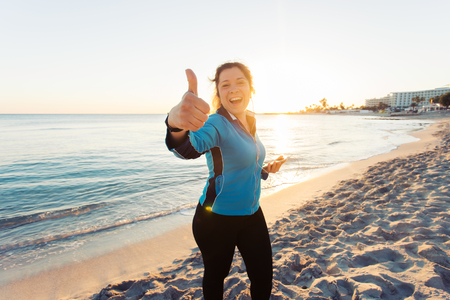 Motivated sporty woman doing thumbs up success gesture after urban workout on seashore.の写真素材