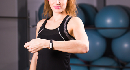 sport, fitness, technology and people concept - young woman with activity tracker and smartphone in gym close-upの写真素材