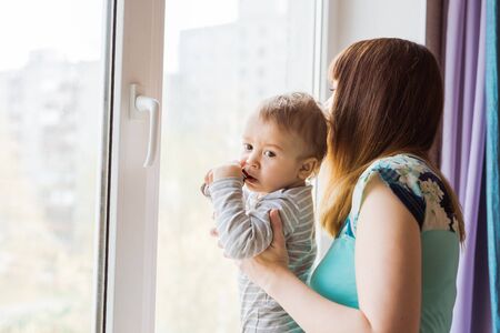 Loving mother playing with her baby son near a windowの写真素材