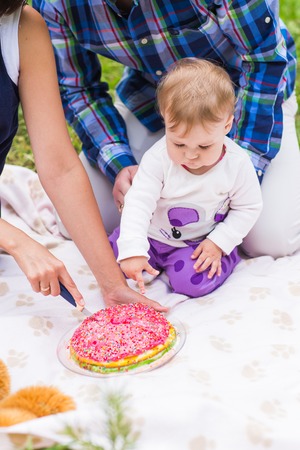Happy young mother and father with their baby daughter relaxing on a blanket in a park celebrating with birthday cakeの写真素材