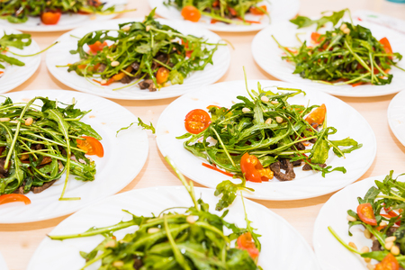 Many plates with fresh salad with meat, tomatoes, nuts and mixed greens arugula, mesclun, mache on the table. Healthy food.の写真素材
