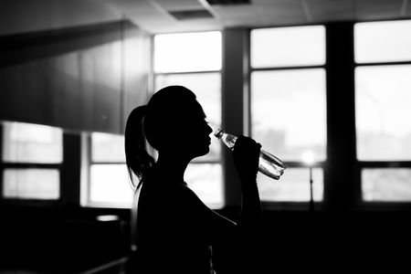 Resting time. Silhouette of sporty girl drink water. Photo of fitness model. Health concept.の写真素材