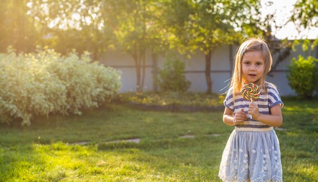 cute little girl eating a lollipop on the grass in summertime.の写真素材