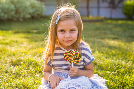 cute little girl eating a lollipop on the grass in summertime.の写真素材