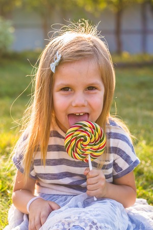Funny child with candy lollipop, happy little girl eating big sugar candy.の写真素材