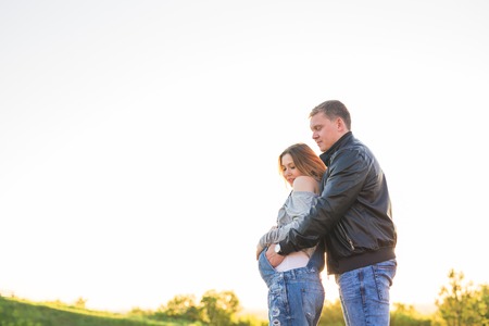 Happy young pregnant couple hugging in natureの写真素材
