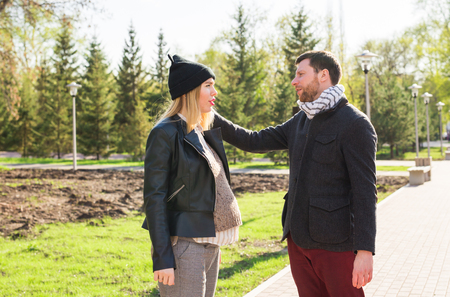 Stylish pregnancy concept - portrait of couple of hipsters husband and wife in trendy clothes walking in the city parkの写真素材