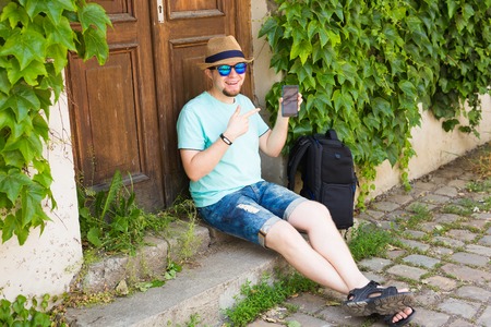 Cheerful man holding and pointing smartphone outdoorの写真素材