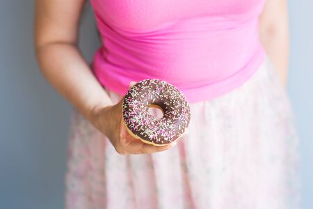 Close-up of woman holds chocolate donut cake. Unhealthy junk food concept on blue backgroundの写真素材