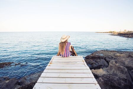 Young happy woman sitting on wooden pier, rear view.の写真素材