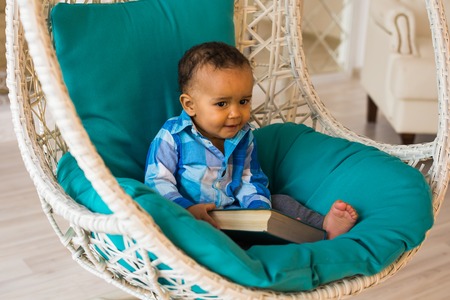 Portrait of African American baby boy holding book on sofa