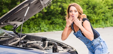 Broken car, accident, feeling confusion and people concept. Portrait of embarrassed young woman with broken car.の写真素材