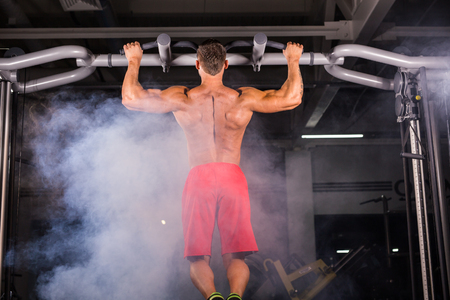 Rear view of muscular man doing pull ups at the gym